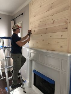 a man standing on a ladder in front of a fireplace with wood paneling over it