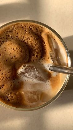 there is a cup of coffee with ice in it on the table next to a spoon