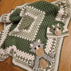 a green and white crocheted blanket sitting on top of a wooden floor next to a stuffed animal