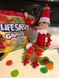 an elf is sitting next to gummy bears and a bag of life - sized gummies