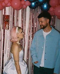 a man and woman standing next to each other in front of balloons