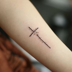 a small cross tattoo on the arm is shown in black and grey ink, with an arrow at the center