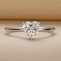 a heart shaped diamond ring sitting on top of a beige cloth