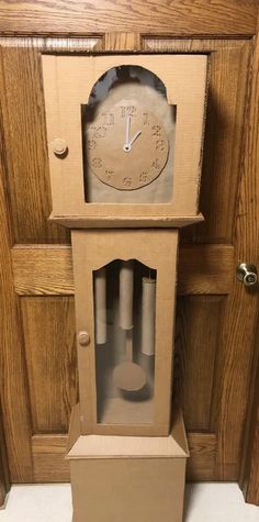 an old clock made out of cardboard sitting on top of a wooden cabinet in front of a door