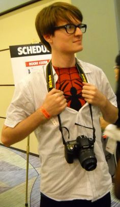 a young man holding a camera and looking at the spiderman shirt on his chest