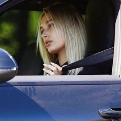 a woman with blonde hair sitting in the passenger seat of a car looking out the window