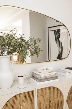 a white vase sitting on top of a wooden table next to a mirror and books