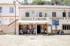 several people sitting at tables in front of a white building with orange and blue trim