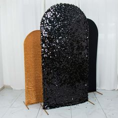 two black and gold sequins on display in front of a white curtained wall