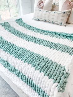 a white and blue blanket on top of a bed next to two pillows with green trim