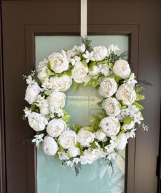 a wreath with white flowers is hanging on the front door to greet someone's guests