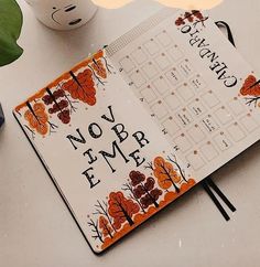 an open notebook sitting on top of a table next to a cup and planter