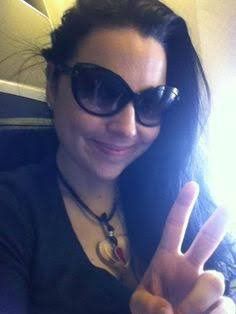 a woman in sunglasses making the peace sign with her hand while sitting on an airplane