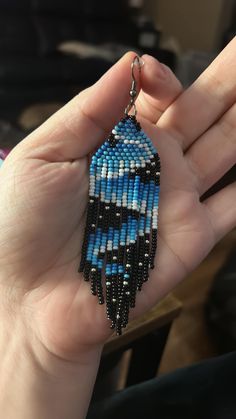 a hand holding a blue and black beaded earrings