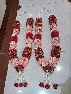 two necklaces made out of flowers and pearls on a marble floor in front of a wall