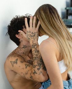 a man and woman kissing each other in front of a wall with tattoos on their arms