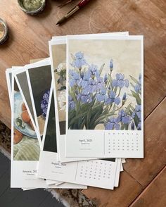 several pictures of blue flowers on a wooden table next to paint brushes and watercolor paints