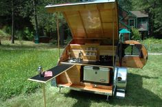 an outdoor kitchen made out of wood in the middle of some grass with trees in the background