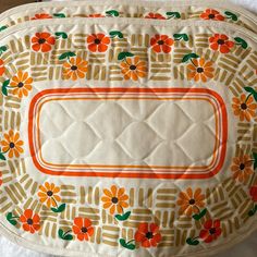 an orange and green floral design on a white quilted placemat with gold trim