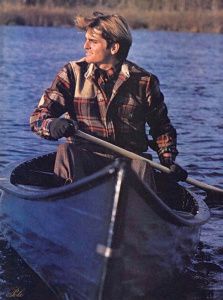 a man in a plaid shirt paddling a canoe