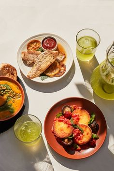 there are three plates with food on them next to two glasses filled with liquids