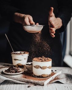 a person sprinkling chocolate on top of a cake in front of other desserts