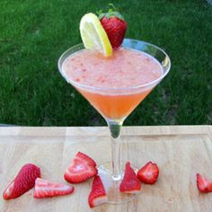 a drink with strawberries and lemon wedges on a table in front of grass