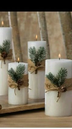 four white candles with pine cones and burlocks tied in twine on a wooden tray