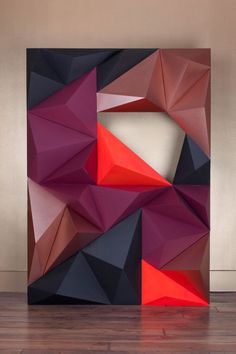 an art piece is displayed on the floor in front of a wall with red and black shapes