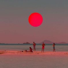 three people standing on the beach with an orange ball in the sky