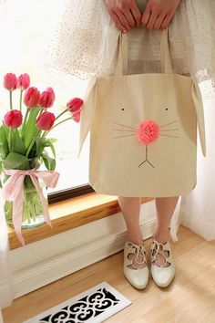 a person holding a bag with a cat face on it and flowers in the background