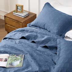 a blue comforter on a bed next to a night stand with a magazine laying on it