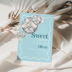 a blue and white sweet sixteen birthday party card on a bed with feathers in the background