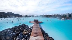 people are swimming in the blue lagoon with wooden walkway