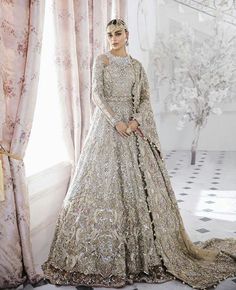 a woman standing in front of a window wearing a wedding dress with an elaborate design