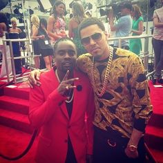 two men standing next to each other on a red carpeted area with stairs and people in the background