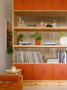 an orange bookcase filled with lots of books next to a chair and potted plant