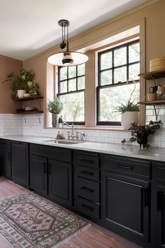 a large kitchen with black cabinets and white counter tops, along with potted plants on the window sill