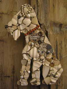 a dog made out of shells and other things on a piece of wood with a tag attached to it