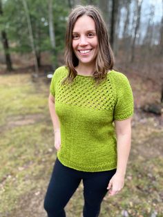 a woman standing in the woods wearing a green knitted sweater and black leggings