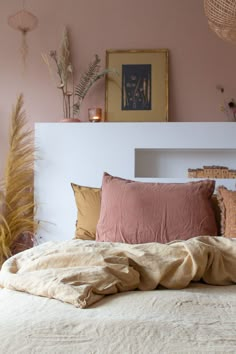 an unmade bed with pink walls and plants on the headboard in front of it