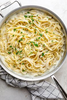 a pan filled with pasta and parsley on top of a white table cloth next to utensils