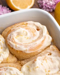 a white dish filled with lemon rolls and frosting next to some sliced oranges