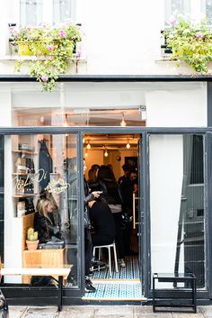 people sitting at tables in front of a store window with flowers on the windowsill