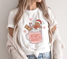 a woman wearing a white t - shirt that says merry and has a teddy bear in a cup