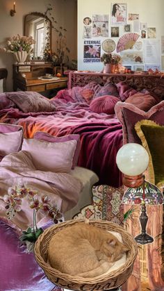 a cat curled up on a bed in a room with purple sheets and pillows, next to a wicker basket