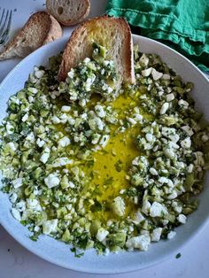 a white bowl filled with food next to bread on top of a table and green napkin