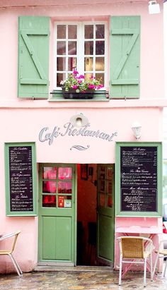 a pink building with green shutters on the outside and tables in front of it