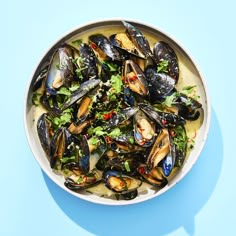 a white bowl filled with mussels and greens on top of a blue surface