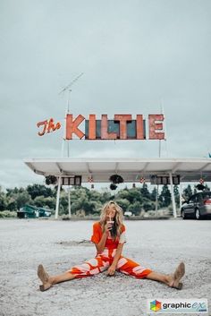 a woman sitting on the ground in front of a sign that says the kiltie